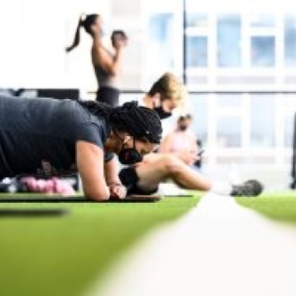 Individuals working out in a gym sitting on the ground stretching