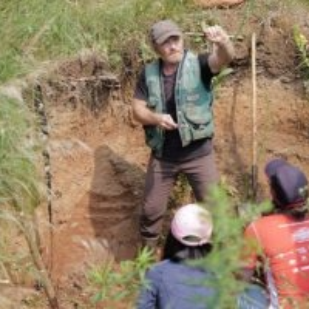 Instructor in a soil pit providing instruction to students sitting on the edge of that soil pit