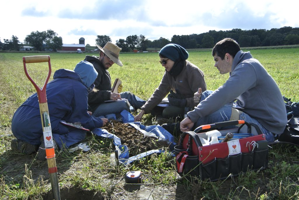 Four students sitting in the field testing soil that had been dug up from the ground